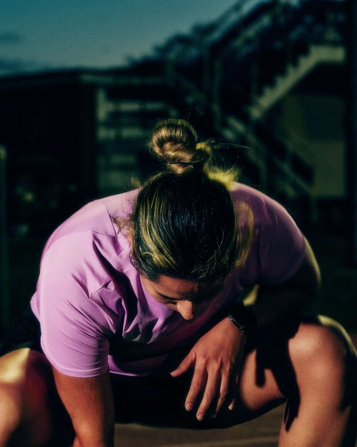 Athlete wearing a pink shirt crouching down in low-light outdoor night setting for Nike