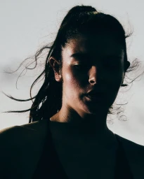 Close-up portrait of a woman in deep shadow against a bright sky, her hair blowing in the wind, shot by Carina Lammers for Nike.