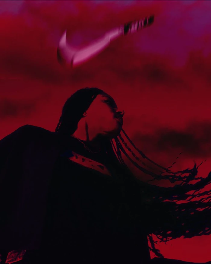 Low angle shot of a woman with braided hair against a dramatic red sky with a floating Nike swoosh logo