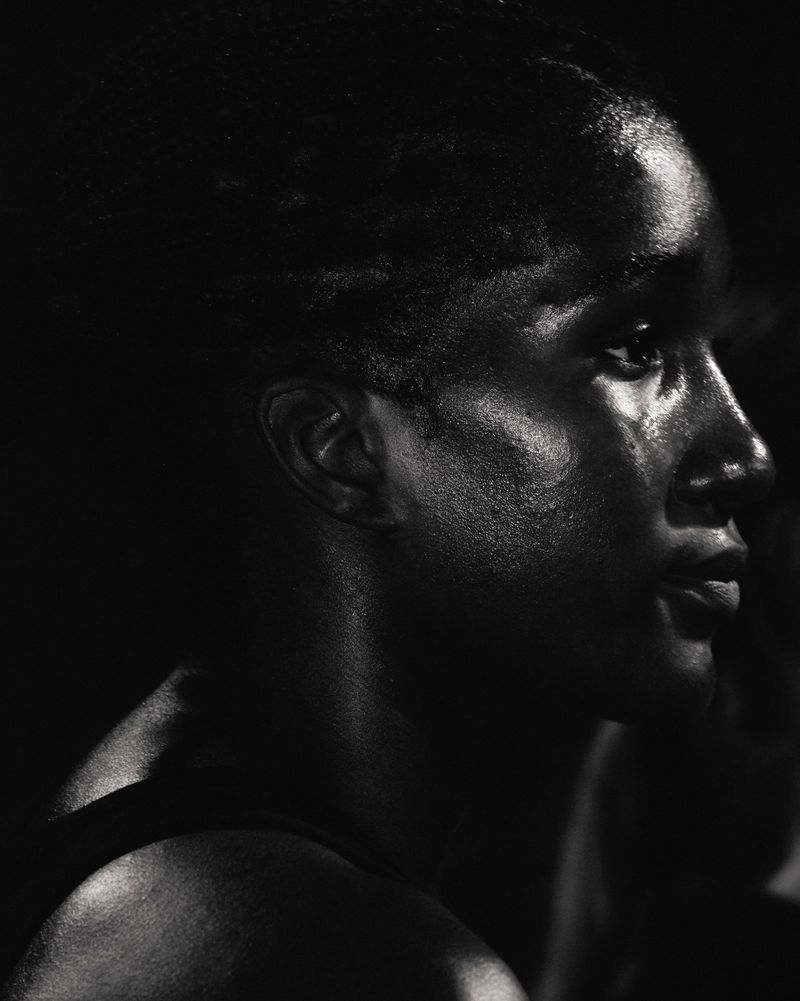Close-up profile portrait of a black woman with sweat on her face under dramatic low-key lighting for Nike After Dark.