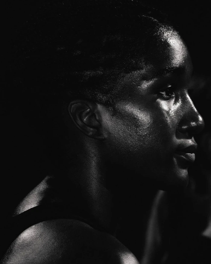 Close-up profile portrait of a black woman with sweat on her face under dramatic low-key lighting for Nike After Dark.