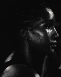 Close-up profile portrait of a black woman with sweat on her face under dramatic low-key lighting for Nike After Dark.