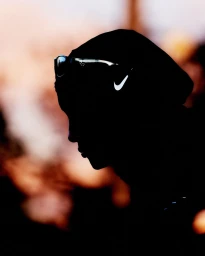 Silhouette profile of a runner wearing a hooded top and sunglasses against a warm dusk background with a visible Nike swoosh logo