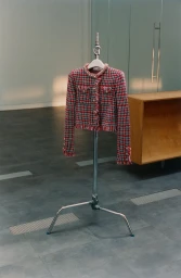 Red and blue tweed jacket displayed on a metal c-stand inside an interior space with wooden cabinetry
