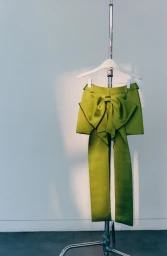Green skirt with a large bow hanging on a clothing rack against a plain white wall