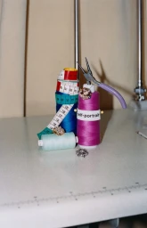 Spools of colorful thread, a measuring tape, pliers, and sparkling jeweled embellishments arranged on a sewing machine table.