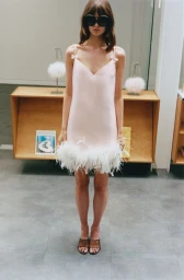 Model wearing a pink slip dress with a feather hem and oversized black sunglasses standing in a showroom