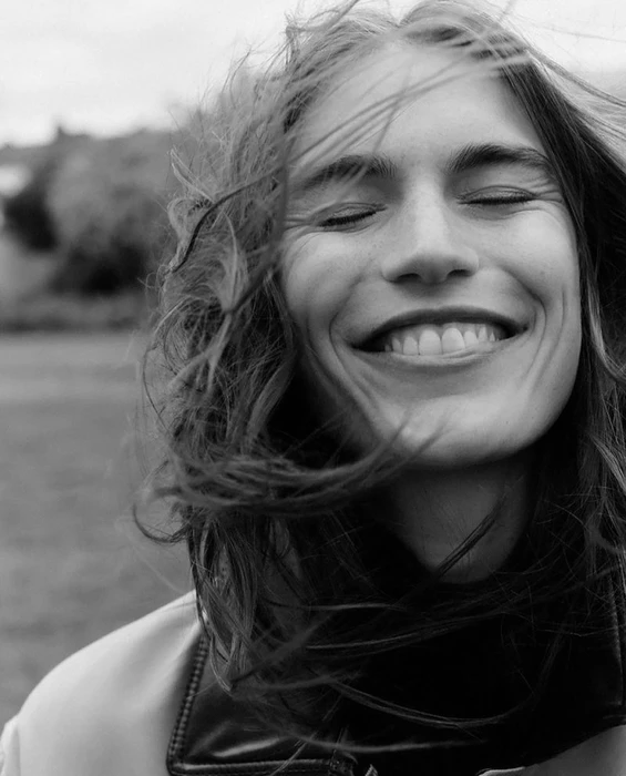 Close-up portrait of model Steffi Cook smiling with closed eyes and wind-blown hair for the Coccinelle AW26-27 campaign.