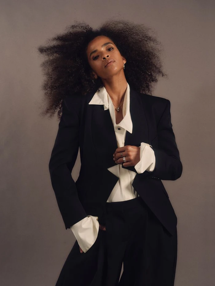 Ramla Ali wearing a dark suit jacket and white shirt against a neutral background for Elle UK, photographed by Sharif Hamza.