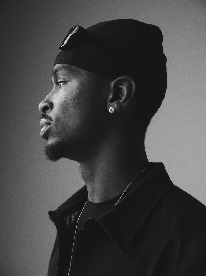 Black and white profile portrait of Shai Gilgeous-Alexander wearing a dark cap and jacket against a plain background