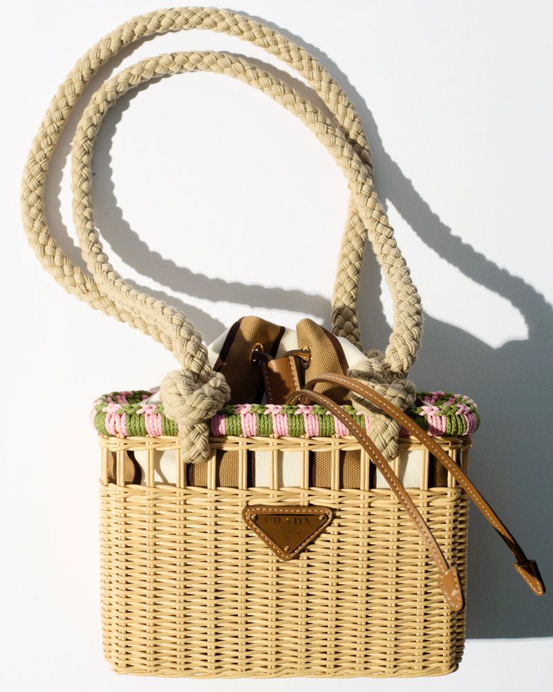Wicker Prada handbag with rope handles, brown leather accents, and a pink and green trim against a white background. Fashion accessory.