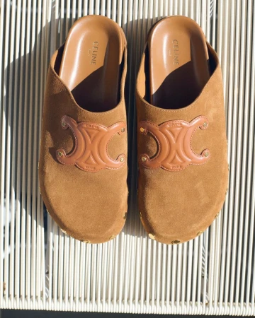 Tan suede Celine mules featuring the brand's Triomphe logo. The photograph showcases the details of the shoes.