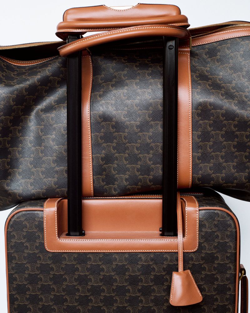Luxury luggage set featuring a rolling suitcase and duffel bag, both adorned with a repeating dark brown monogram pattern and tan leather trim.