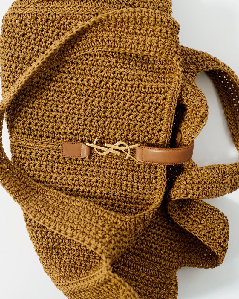 Crochet hobo bag in brown with a tan leather belt featuring a gold YSL logo buckle, set against a clean, bright white backdrop.