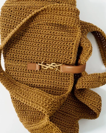 Crochet hobo bag in brown with a tan leather belt featuring a gold YSL logo buckle, set against a clean, bright white backdrop.