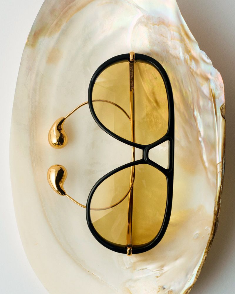 Sunglasses with gold accents on a pearlescent seashell, top-down shot, studio lighting. Fashionable eyewear for summer style.