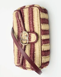 Woven straw shoulder bag with burgundy and cream stripes, burgundy leather strap, and a gold interlocking logo on white background.