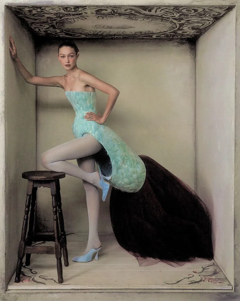 Gigi Hadid posing inside a set-dressed box wearing a structured light blue dress and white tights, photographed by Szilveszter Mako for WSJ.