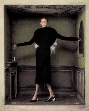 Gigi Hadid standing in a black structured dress with arms outstretched inside a painted miniature room set