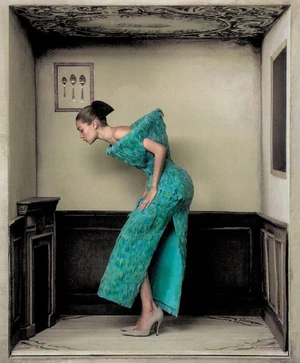 Gigi Hadid posing in a textured turquoise gown inside a miniature room set for a WSJ Magazine editorial feature.