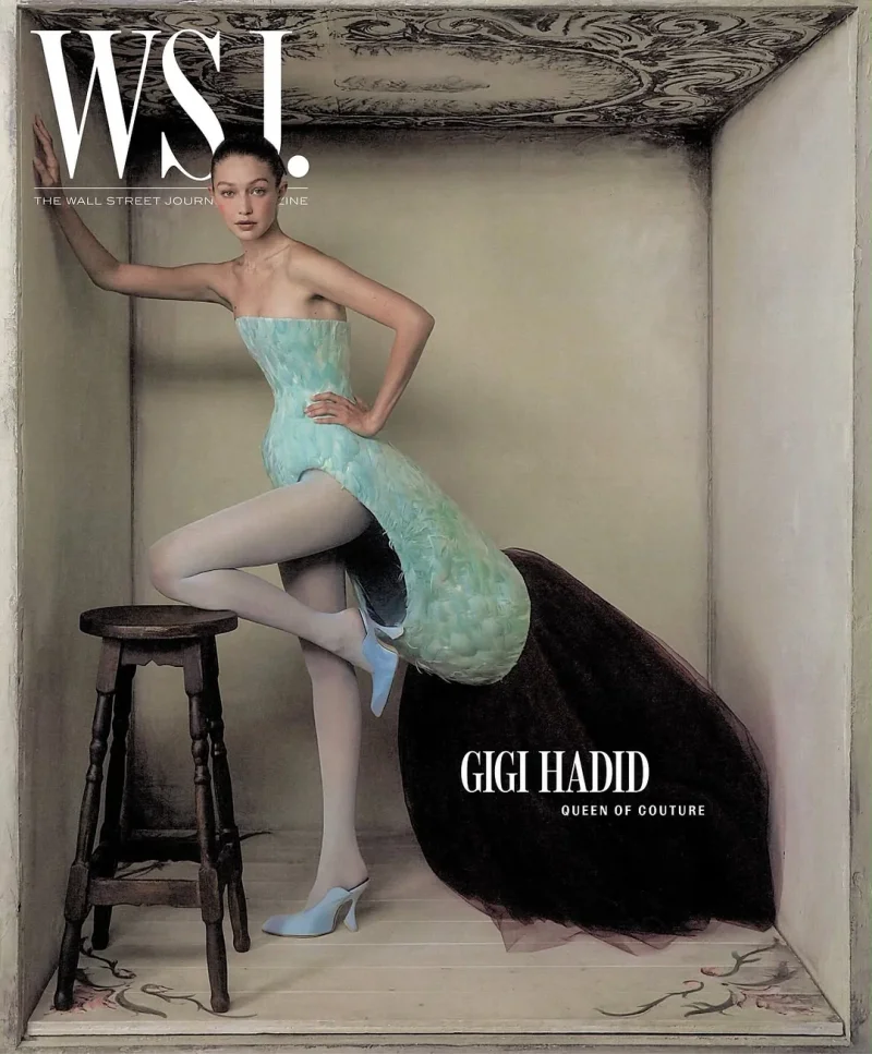 Gigi Hadid posing inside a miniature room set wearing a structured mint green and black sculptural gown with light blue mules.