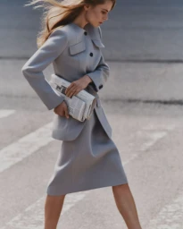 Model walking outdoors wearing a grey tailored jacket and skirt carrying a newspaper, photographed by Dudi Hasson for Helsa.
