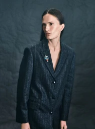 Model wearing a dark pinstripe blazer with a small brooch against a textured grey background for Harper's Bazaar Germany