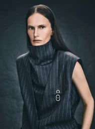 Model in grey pinstripe high-collared sleeveless vest against dark textured background