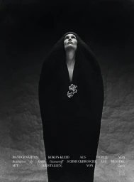 Model in a black hooded wool coat with a crystal brooch looking upward against a textured dark background
