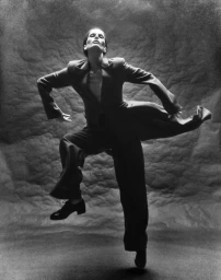 Model in grey suit jacket and trousers leaping mid-air against a textured grey studio backdrop