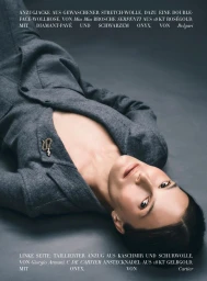 Model lying on a grey studio backdrop wearing a grey wool suit jacket with a small serpent brooch.