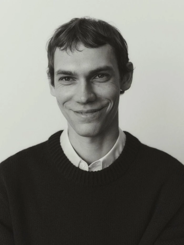 Portrait of Aleksandr Gordeev wearing a dark sweater and white shirt against a neutral background for Arket.