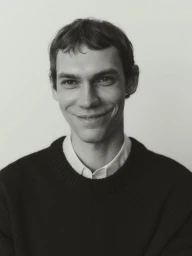 Portrait of Aleksandr Gordeev wearing a dark sweater and white shirt against a neutral background for Arket.