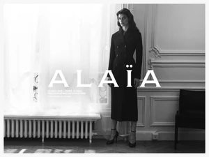 Model Alaina Rae in a dark double-breasted coat standing indoors near a bright window for Alaia by David Sims