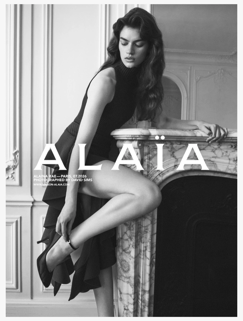 Model Alaina Rae posing by a marble fireplace in a black sleeveless dress for Alaia, photographed by David Sims.