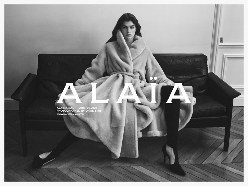 Model Alaina Rae seated on a leather sofa wearing a belted plush coat for Alaïa photographed by David Sims.