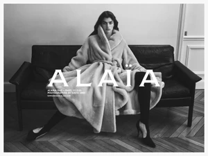 Model Alaina Rae seated on a leather sofa wearing a belted plush coat for Alaïa photographed by David Sims.