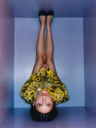 Inde Navarrette inverted in a box wearing a yellow floral patterned shirt and black flats for W Magazine