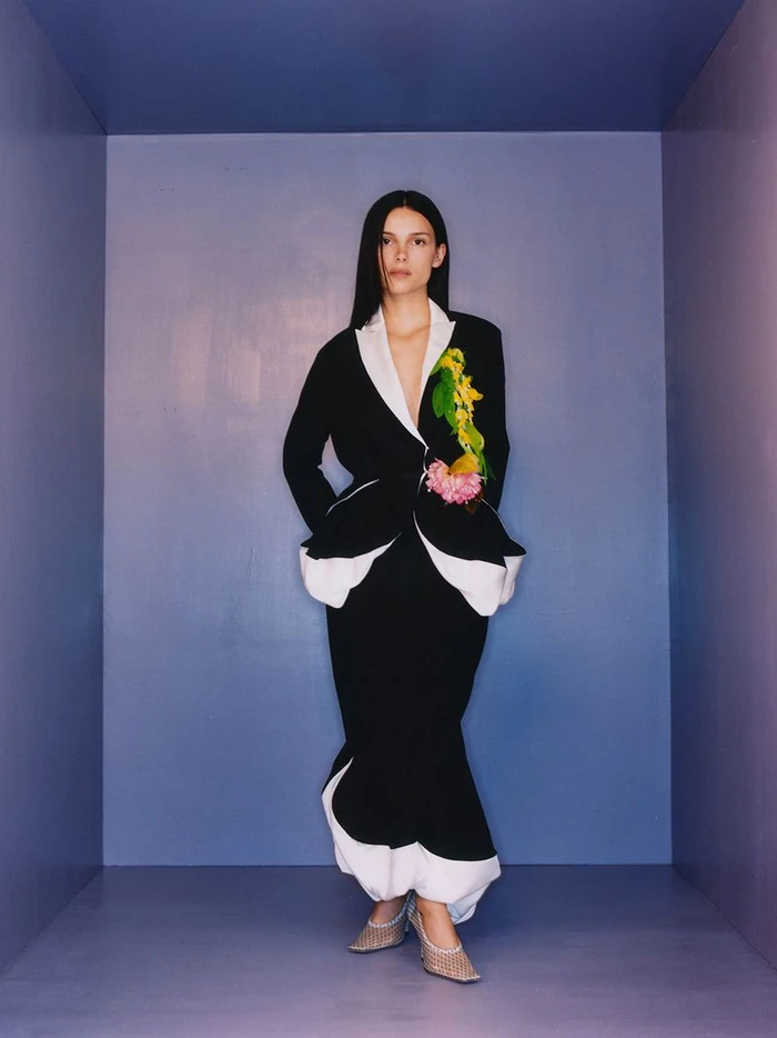 Inde Navarrette standing inside a blue alcove wearing a black and white tailored suit with floral details for W Magazine.