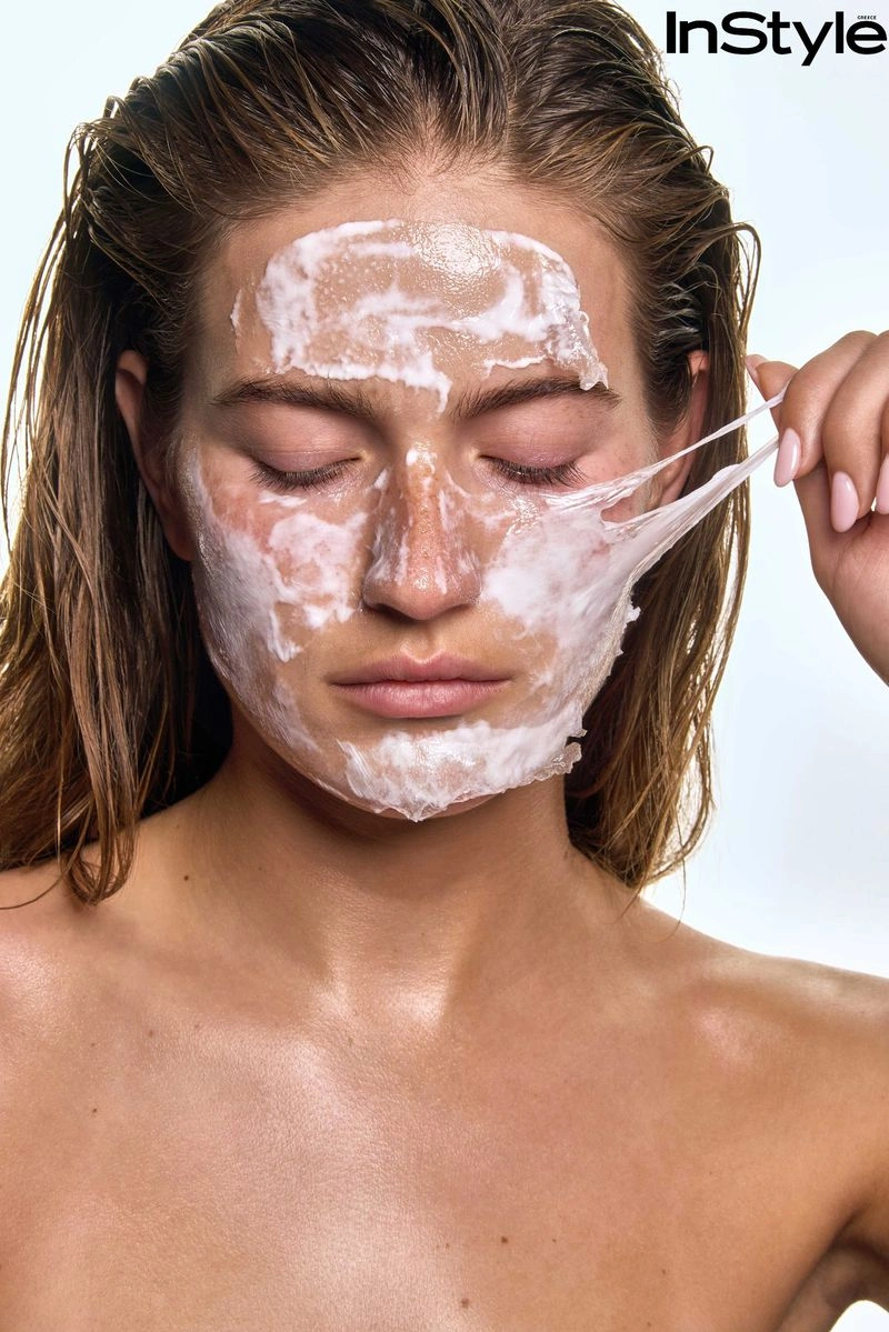 Close-up portrait of a woman peeling a white face mask off her skin for an InStyle Greece skincare editorial.