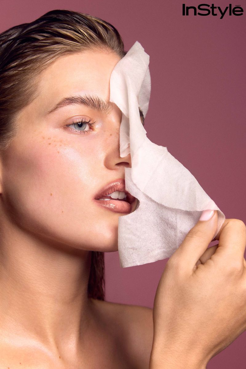 Close-up of a model peeling off a white face mask sheet against a muted pink background for InStyle Greece.