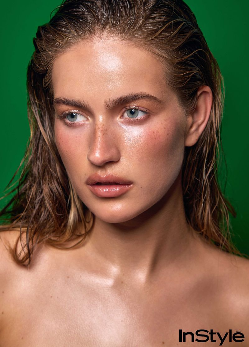 Close-up portrait of a woman with wet hair and glowing skin against a green backdrop for InStyle Greece skincare