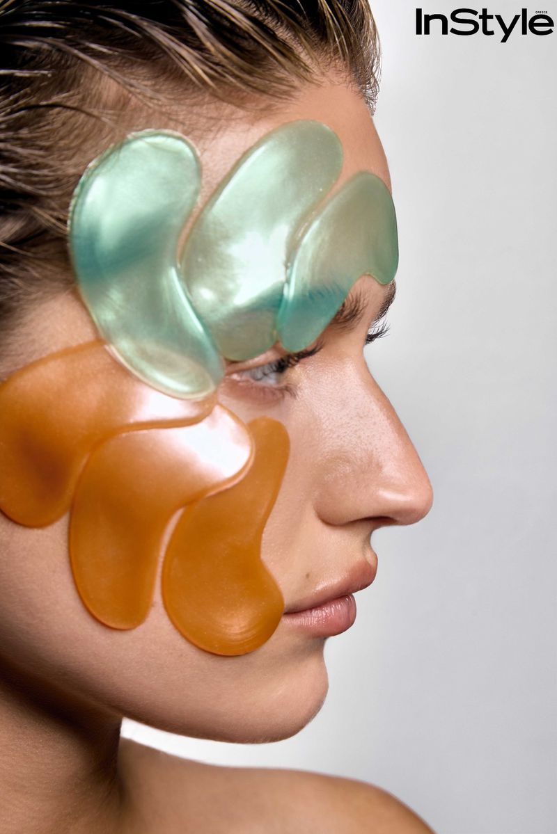 Profile portrait of a woman wearing glossy mint green and orange skincare patches on her face against a white background