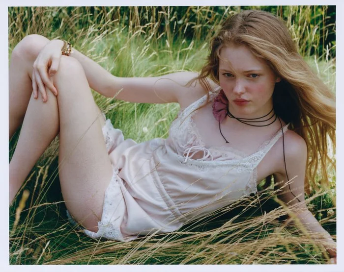 Model Ava Shipp lounging in tall grass wearing a pale pink silk slip dress for Revolve editorial Second Nature by Agata Serge.
