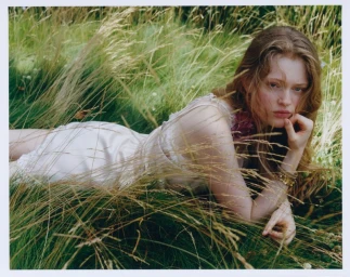 Model lying in tall grass wearing a light-coloured dress and gold bracelets