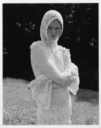 Model Ava Shipp in a white lace hooded dress posing outdoors in a grassy field for the Revolve Second Nature editorial.