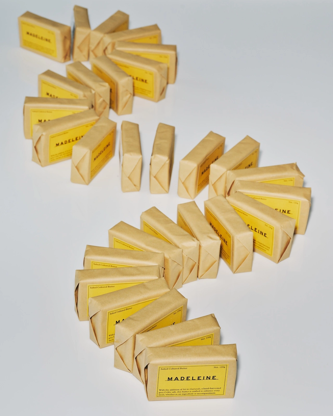 A winding arrangement of brown paper-wrapped rectangular packages with yellow labels featuring the brand name Madeleine.