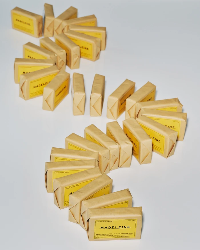 A winding arrangement of brown paper-wrapped rectangular packages with yellow labels featuring the brand name Madeleine.