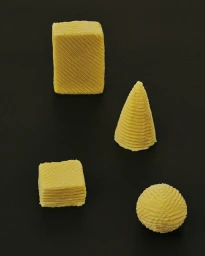 Four textured yellow geometric shapes including a cube, cylinder, square block, and sphere arranged on a dark background.