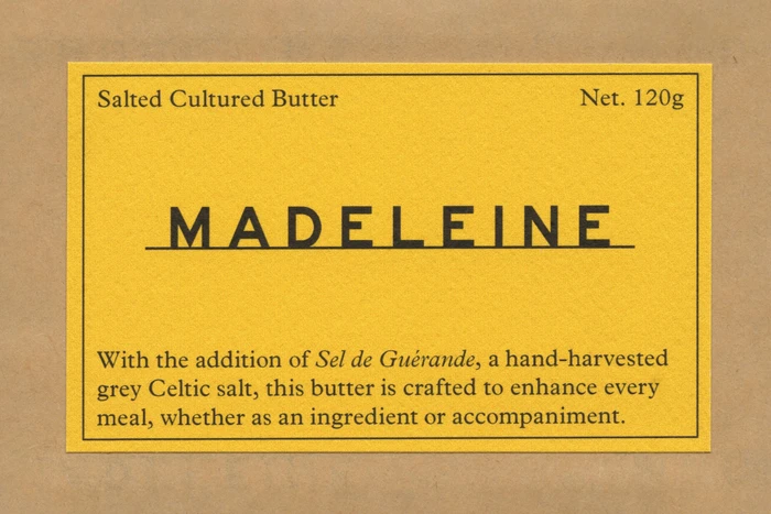 Yellow product label with black typography for Madeleine butter centered on textured brown paper.